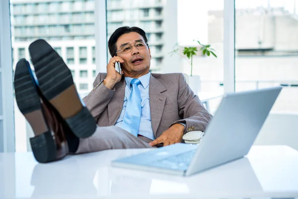 Uomo d'affari al telefono con i piedi sulla scrivania — Foto Stock