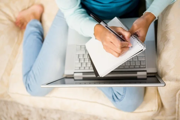 Femme écrit sur un bloc-notes avec ordinateur portable — Photo