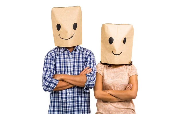 Couple with arms crossed wearing smiley paper bags — Stock Photo, Image