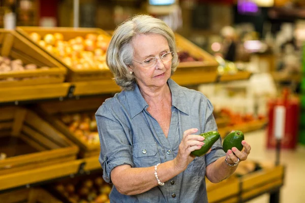 Старшая женщина держит два авокадо — стоковое фото
