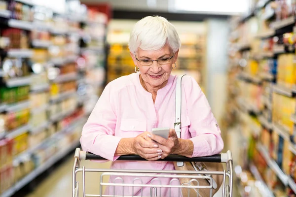 Senior woman using phone while pushing cart — Stock Photo, Image