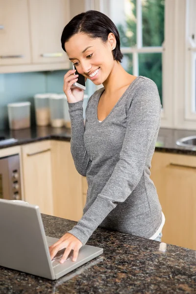 Morena sorridente no telefonema usando laptop — Fotografia de Stock