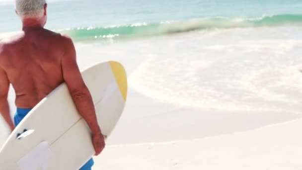 Alter Rentner geht mit Surfbrett an den Strand — Stockvideo