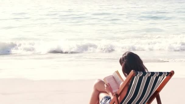 Morena leyendo un libro en cubierta silla — Vídeos de Stock