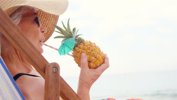 Mulher aposentada bebendo coquetel e deitada na cadeira de praia — Vídeo de Stock