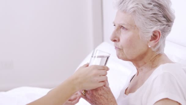 Enfermera sonriente dando agua a la mujer mayor en la cama — Vídeos de Stock