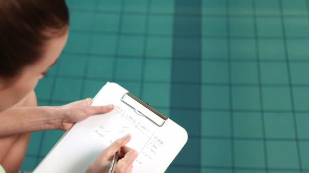 Treinador feminino escrevendo notas por piscina — Vídeo de Stock
