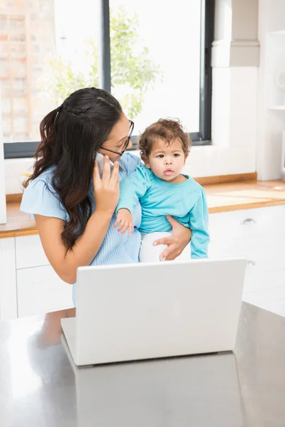 Bruna che tiene il bambino e utilizza il computer portatile — Foto Stock