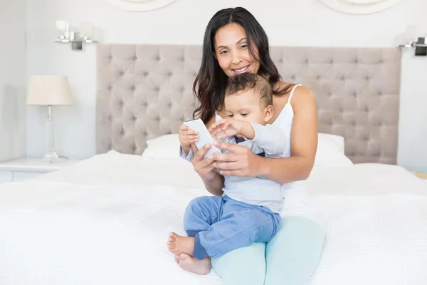 Brünette hält Baby und nutzt Smartphone — Stockfoto