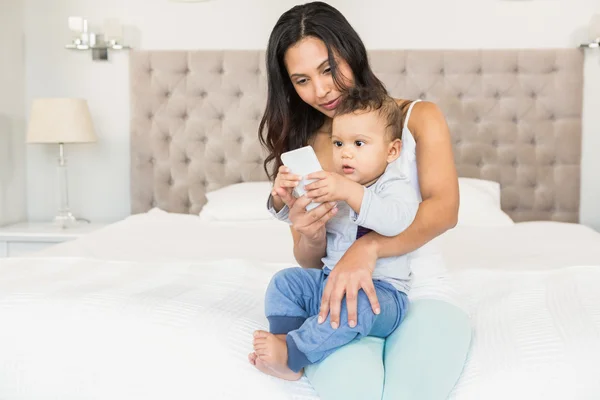 Brunette holding baby and using smartphone — Stock Photo, Image