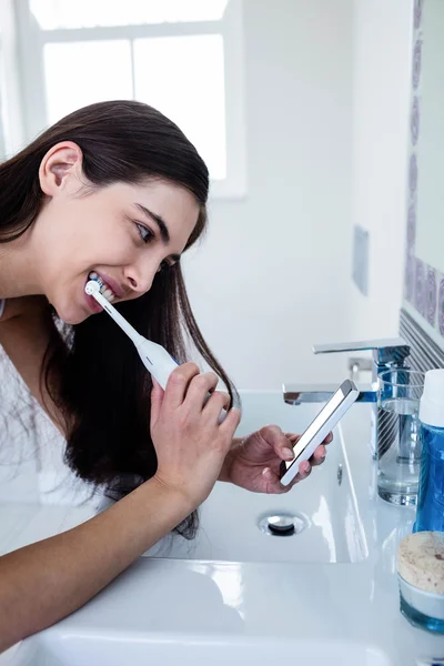 Брюнетка с помощью смартфона при чистке зубов — стоковое фото
