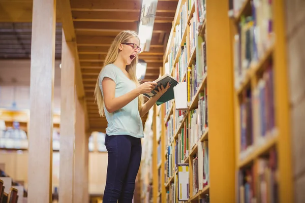 Student reading book next to bookshelf — 图库照片