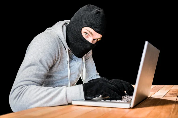 Focused thief with hood typing on laptop — Stock Photo, Image