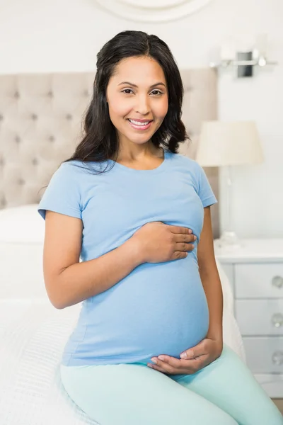 Gravid brunett sitter på sängen — Stockfoto