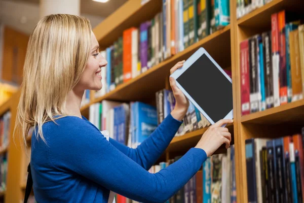 Студент убирает планшет в книжной полке — стоковое фото