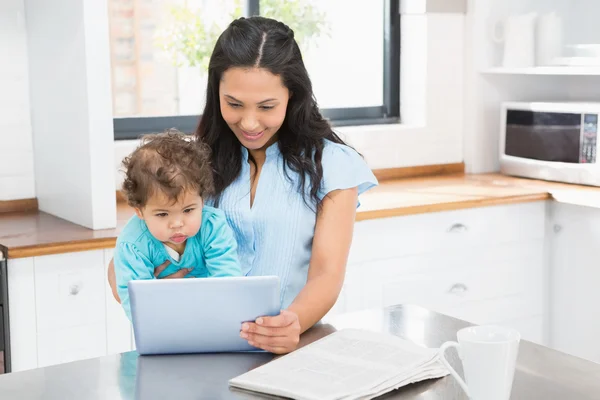 Brünette hält Baby und benutzt Tablette — Stockfoto