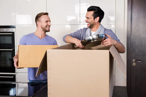 Sorrindo gay casal desembalagem papelão — Fotografia de Stock