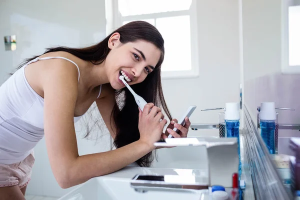 Morena usando smartphone enquanto escova os dentes — Fotografia de Stock