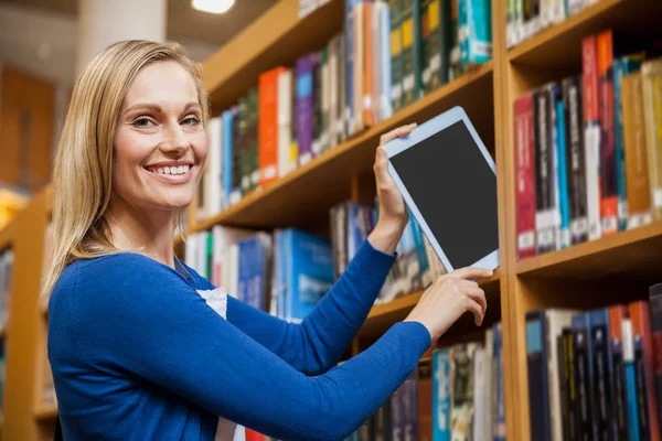 Vrouwelijke student opruimen tablet in boekenkast — Stockfoto