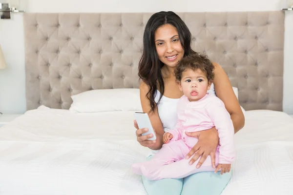 Morena segurando bebê e usando smartphone — Fotografia de Stock