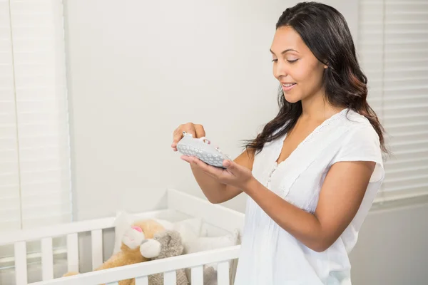 Smiling brunette holding baby shoes — Stock Photo, Image