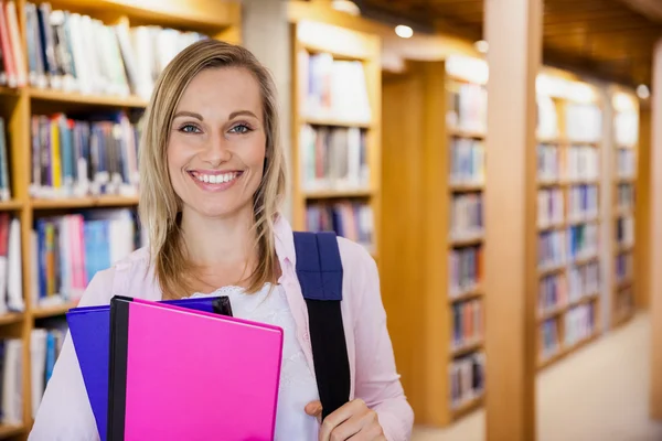 Estudante feminina segurando livros didáticos na biblioteca — Fotografia de Stock