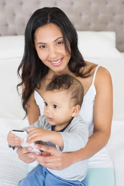 Bruna che tiene il bambino e utilizza smartphone — Foto Stock