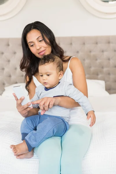 Morena segurando bebê e usando smartphone — Fotografia de Stock