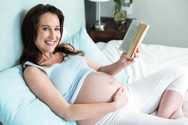 Mujer embarazada en la cama leyendo un libro — Foto de Stock