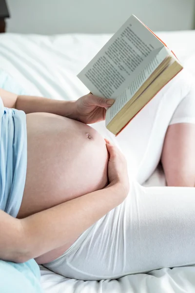 Kobieta w ciąży na łóżku czytając książkę — Zdjęcie stockowe