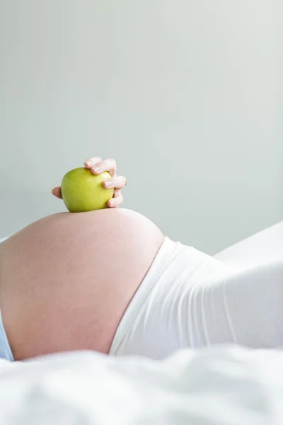 Беременная женщина держит яблоко на животе — стоковое фото