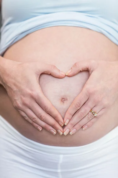 Kobieta w ciąży robi serce z jej ręki na brzuchu — Zdjęcie stockowe