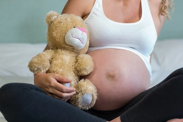 Mujer embarazada sentada con un oso de peluche —  Fotos de Stock