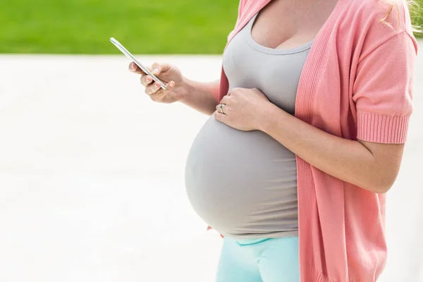 Pregnant woman touching her belly and texting — Stock Photo, Image