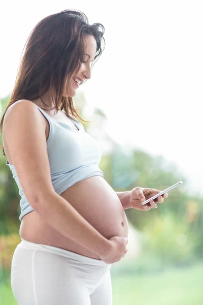Беременная женщина трогает живот и пишет смс — стоковое фото