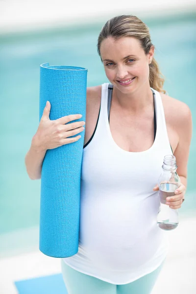 Беременная женщина держит бутылку с водой и коврик — стоковое фото