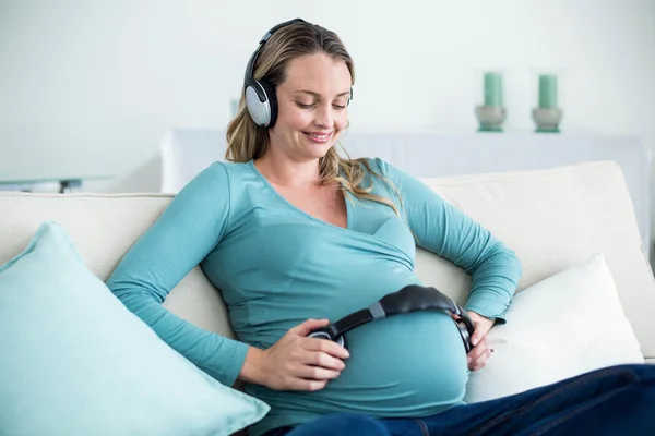 임신한 여자의 배꼽에 헤드폰으로 음악을 듣고 — 스톡 사진