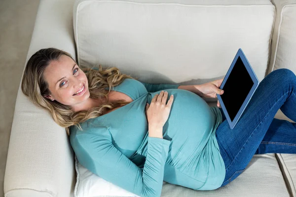 Mulher grávida usando tablet deitado no sofá — Fotografia de Stock