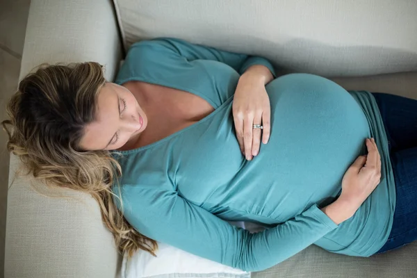 Mulher grávida tocando sua barriga deitada no sofá — Fotografia de Stock