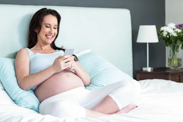 Donna incinta sdraiata a letto a messaggiare — Foto Stock