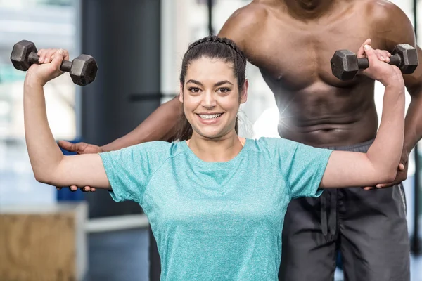 Athletic woman lifting weights helped by trainer — Stock Photo, Image