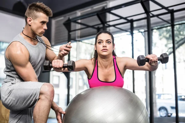 Treinador masculino auxiliando mulher levantando halteres — Fotografia de Stock