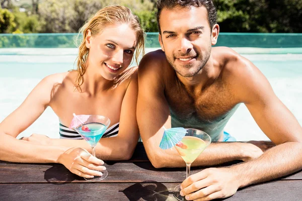 Gelukkige paar leunend op de rand van het zwembad en houden van cocktails — Stockfoto