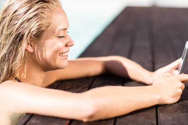Blondýnka se opírá o okraje bazénů a použití smartphone — Stock fotografie