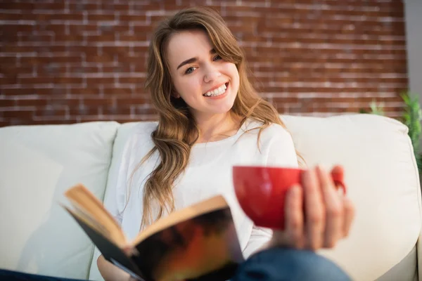 Усміхнена жінка читає книгу під час пиття — стокове фото