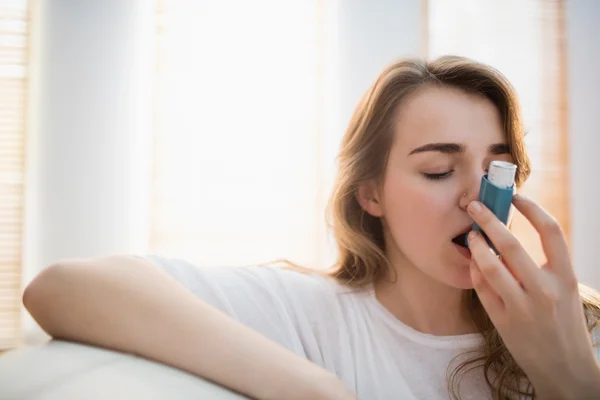 Woman using her inhaler on couch — Stock Photo, Image