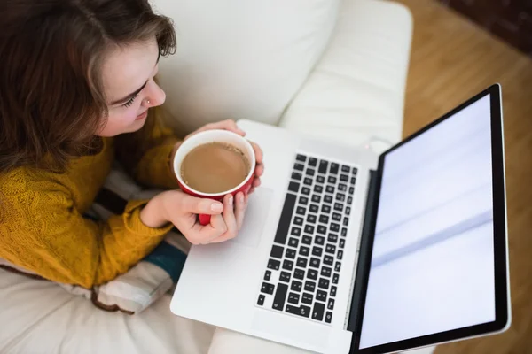 Sonriendo mujer bonita usando el ordenador portátil mientras bebe café — Foto de Stock