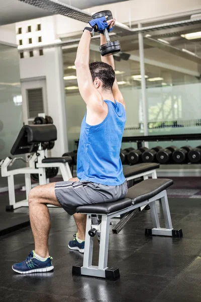 Muskulös man lyft hantel medan du sitter på bänken — Stockfoto