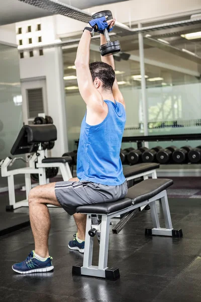 Muscular hombre levantando la mancuerna mientras está sentado en el banco — Foto de Stock