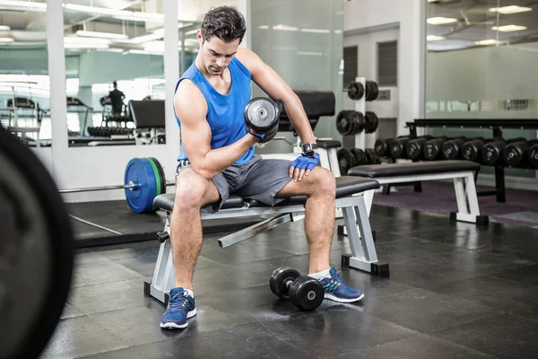 Muscular hombre levantando la mancuerna mientras está sentado en el banco — Foto de Stock